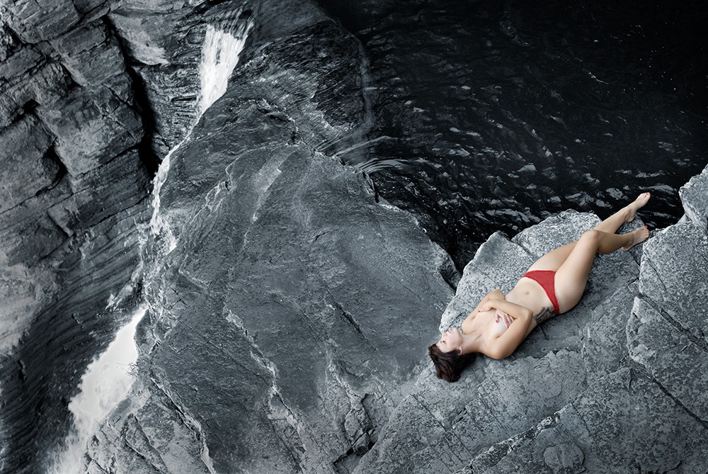 Photographie d’une femme semi-nue dans un décor naturel de rochers / nu féminin et cascade d’eau