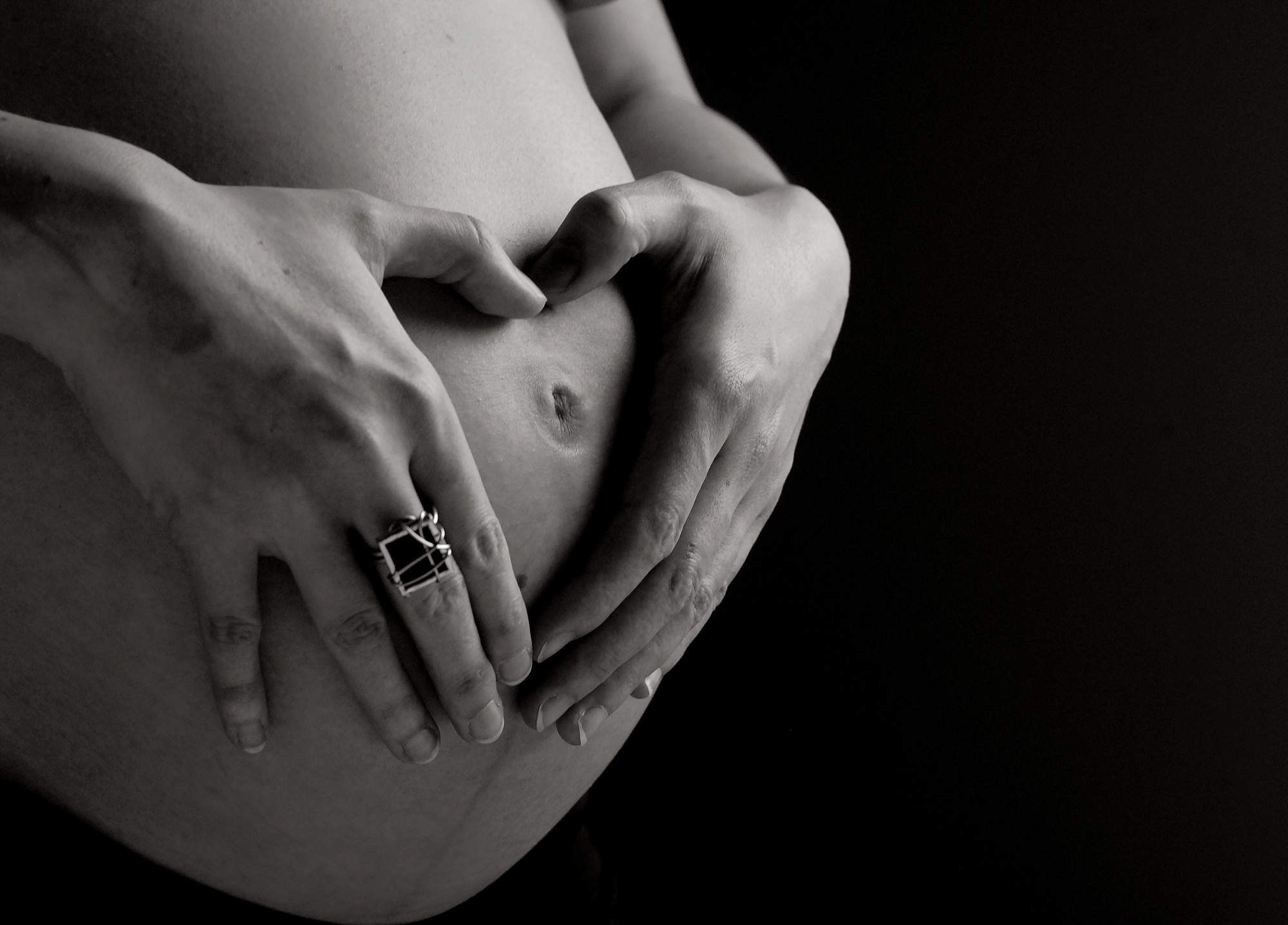 Photo noir et blanc de mains en coeur sur bedaine de femme enceinte / Séance photo de maternité à Québec
